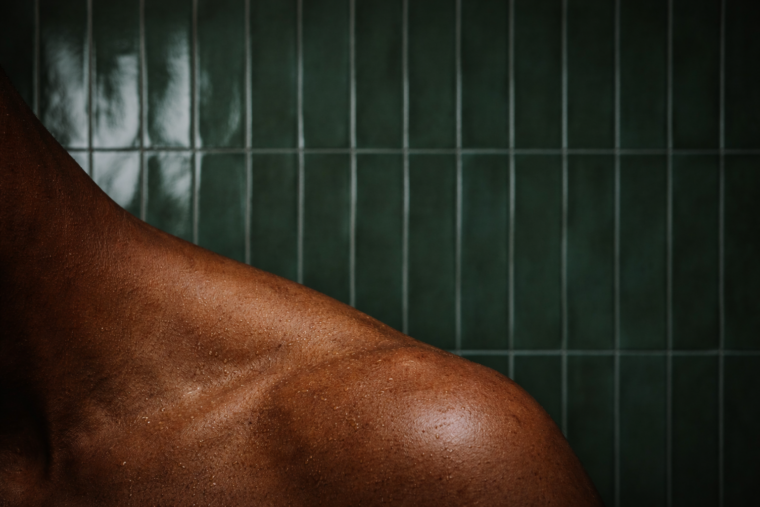 En mans axel med ett mörkt grönt kakel som bakgrund